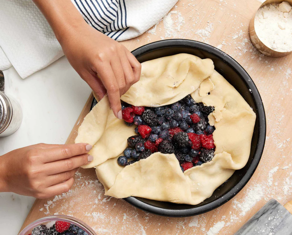 Image of a black, pure ceramic nontoxic pie plate which is free of metals and great for everyday use, from an Xtrema cookware review, a freeform pastry is being folded over fresh berries by a woman's hand.